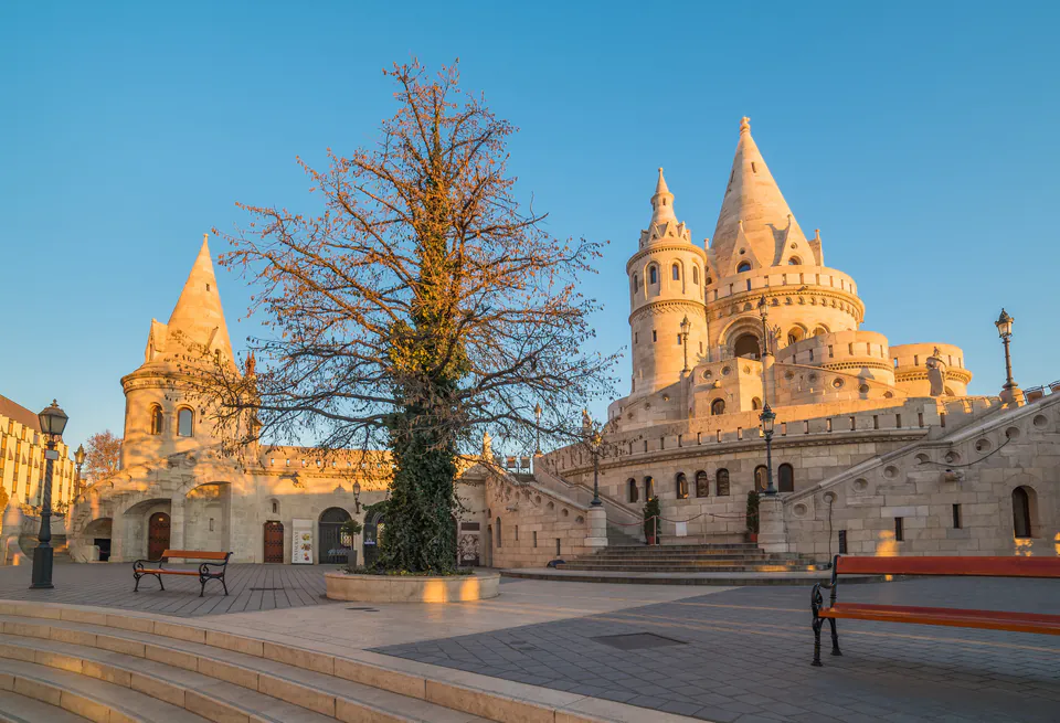 Fisherman's Bastion towers bathed in golden morning light with empty courtyard and bare tree