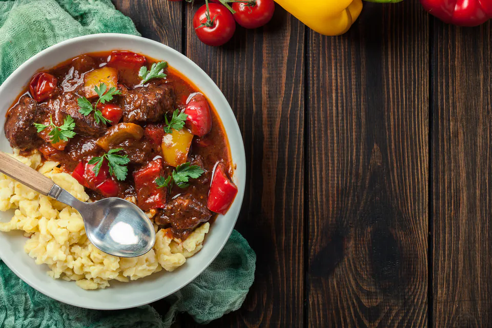 Bowl of rich Hungarian goulash with tender beef, colorful peppers, and herbs served over yellow rice