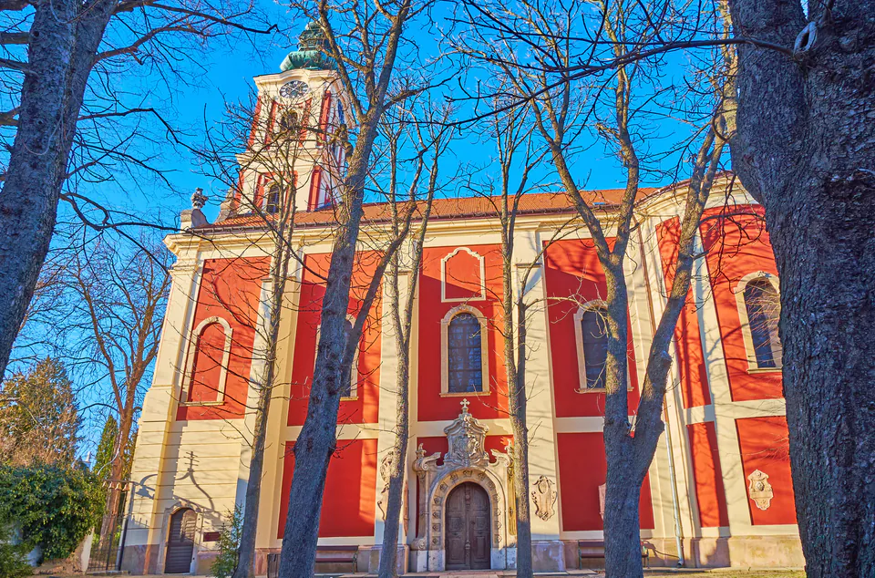 Baroque-style Serbian Orthodox cathedral with red walls and ornate white trim framed by bare winter trees