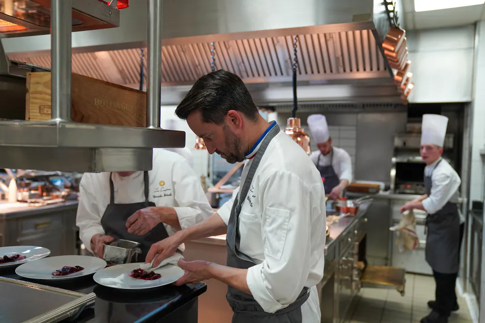 Chef plating dishes in professional kitchen with other chefs working in background
