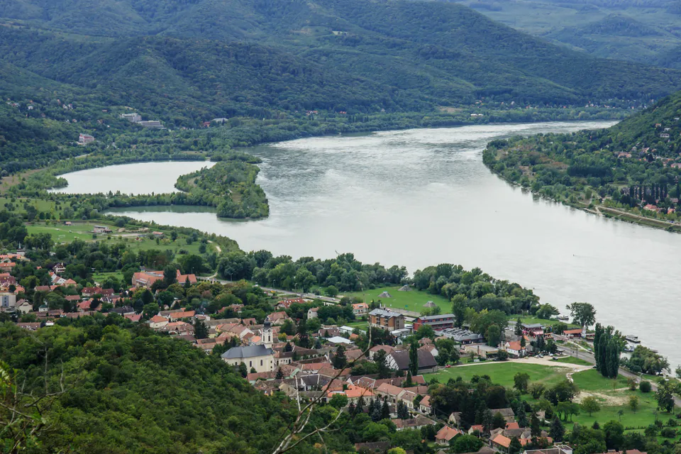 Sweeping view of the Danube River's dramatic bend with forested hills and village nestled along shore