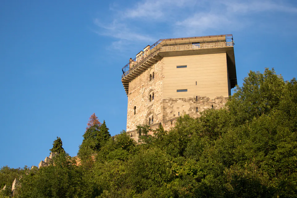 Hexagonal stone tower rising above green trees against blue sky