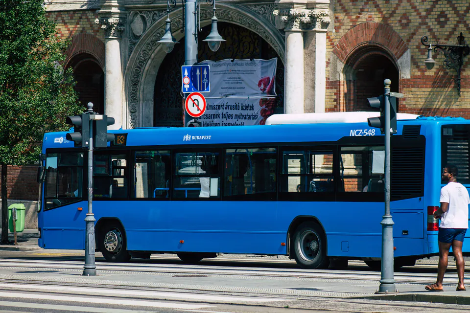 Blue 100E Airport Express bus stopped at a station with ornate architectural backdrop