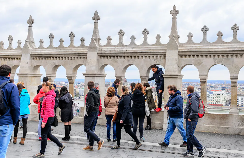 Tour group follows guide along ornate castle terrace overlooking Budapest cityscape