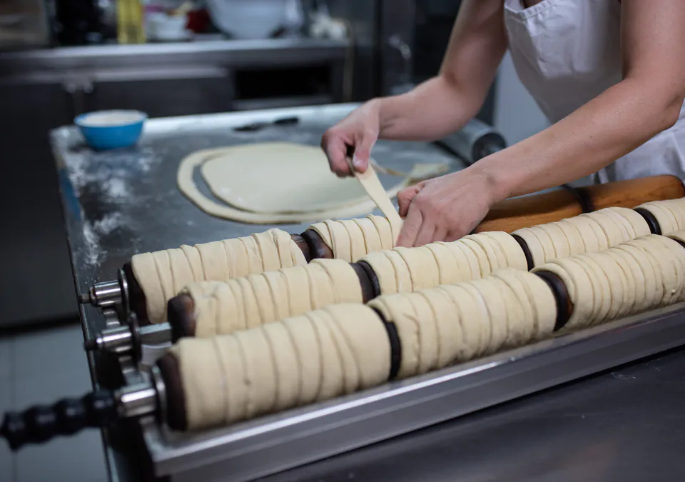 Hands preparing traditional Hungarian pastry dough on rotating spits in professional kitchen