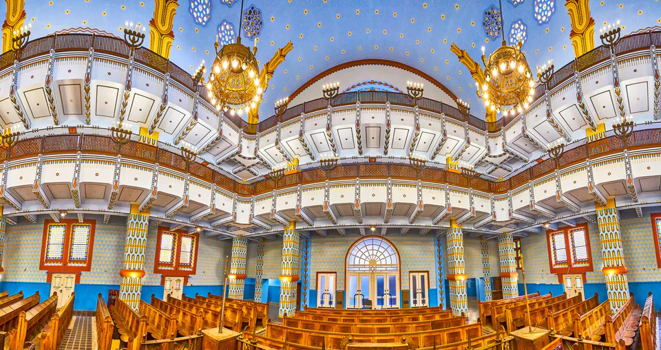 Ornate synagogue interior with blue ceiling, golden chandeliers, and wooden pews