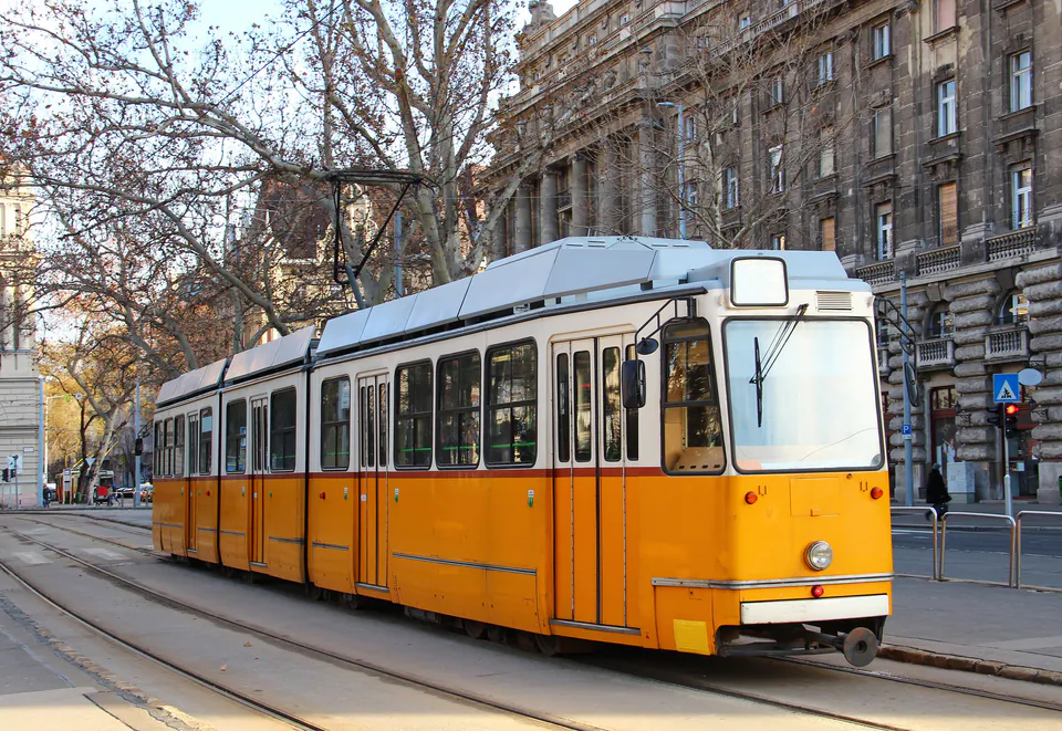 Yellow and white vintage tram on tracks in front of historic Budapest building