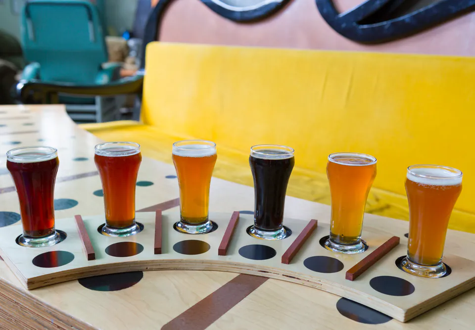 Wooden flight board with six different colored craft beers in tasting glasses