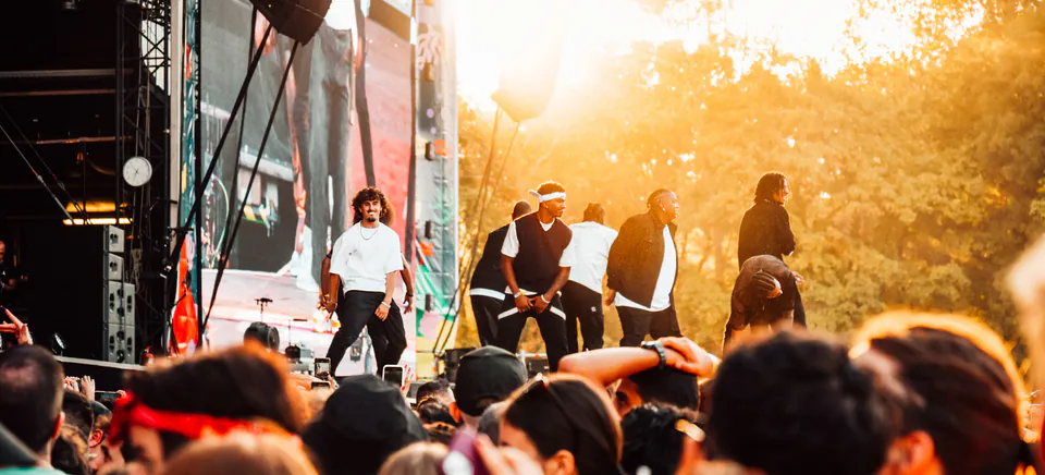 Performers on stage at sunset during a music festival with crowd in foreground
