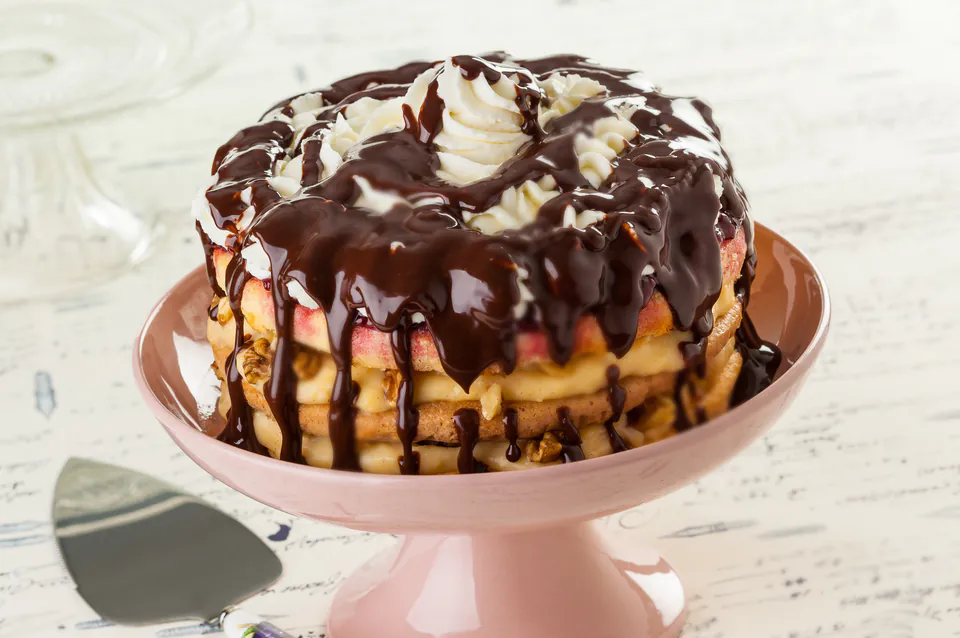 Somlói Galuska dessert layered with sponge cake, whipped cream and chocolate sauce on pink stand