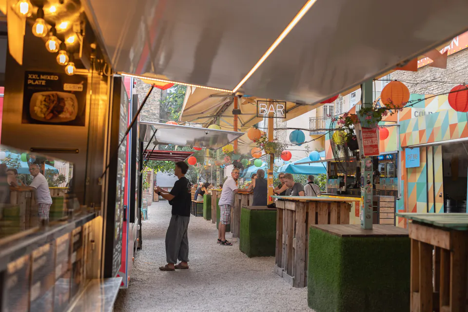 Atmospheric outdoor bar area with string lights, lanterns and patrons at counter seating