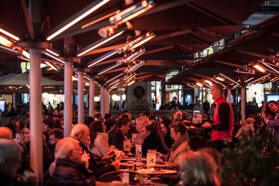 Heated outdoor restaurant terrace filled with diners under red lighting at night