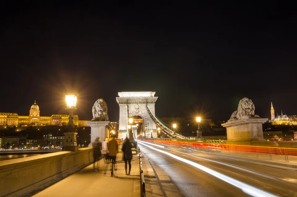 Couple walking hand in hand across illuminated Chain Bridge at night with city lights reflecting in Danube