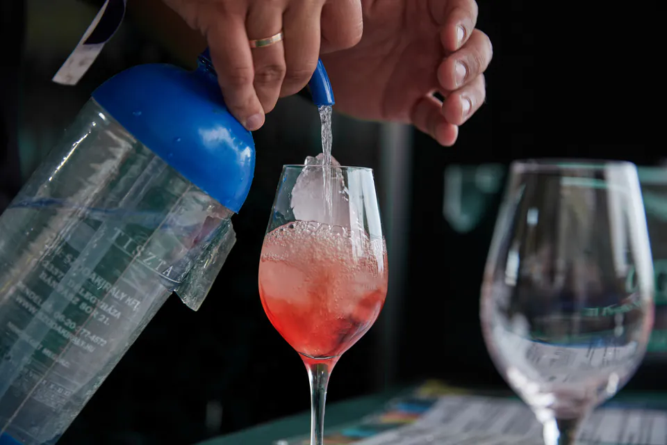 Bartender pouring a pink cocktail from a blue shaker into a wine glass
