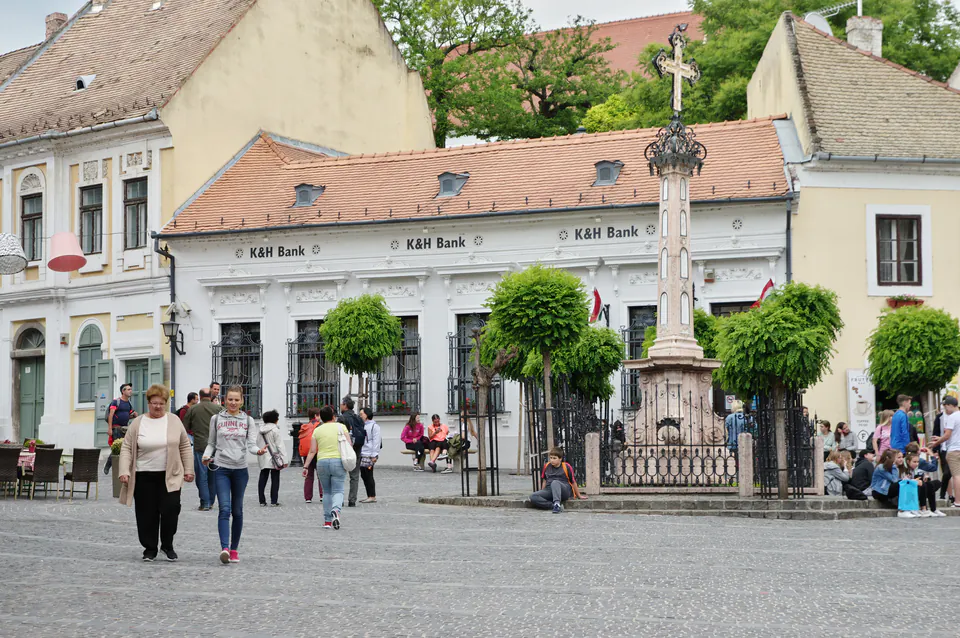 Historic plague cross monument and baroque buildings around Szentendre's main square with visitors walking