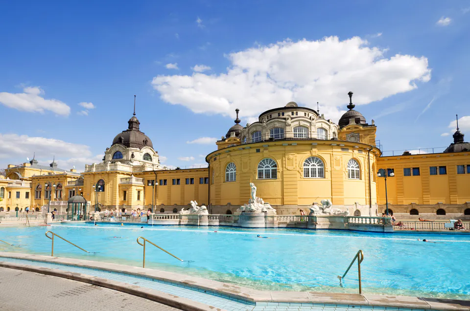 Outdoor pool and neo-baroque yellow facade of Széchenyi Thermal Baths under blue sky