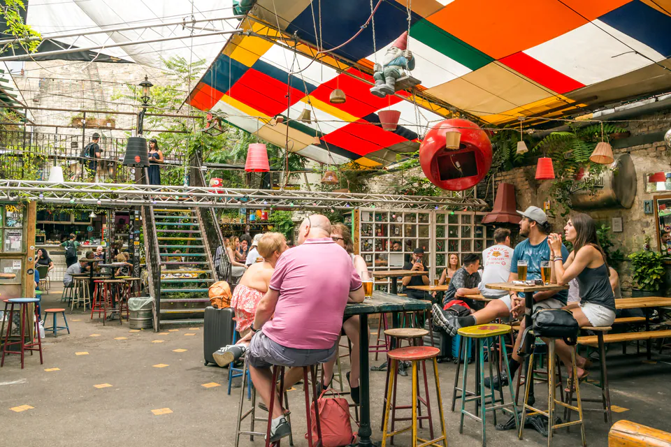 Outdoor courtyard of ruin pub with colorful ceiling panels and people seated at high tables