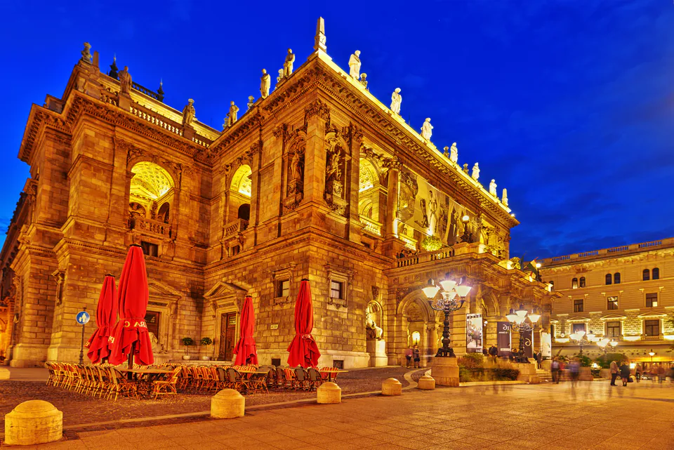 Historic opera house illuminated at night with golden lights and red cafe umbrellas