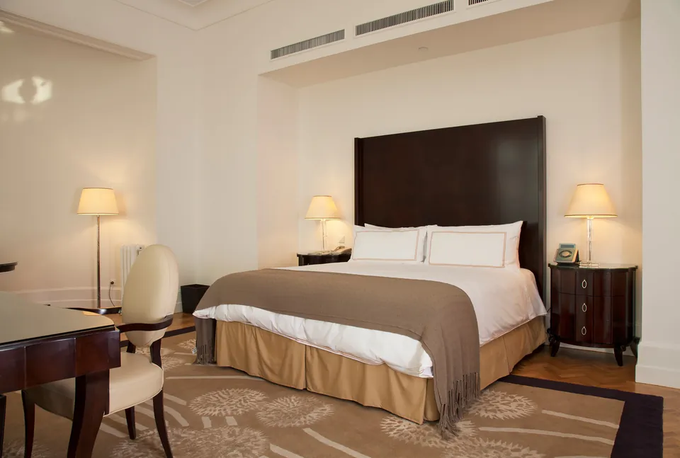 Elegant hotel room with king bed, dark wood furniture, and cream-colored decor