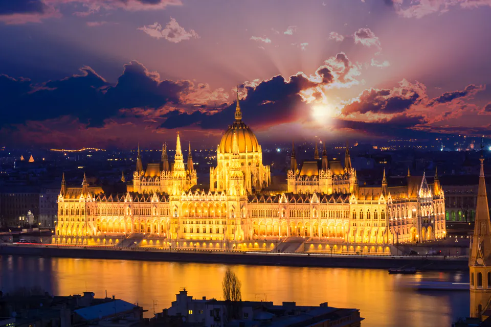 Hungarian Parliament Building illuminated at night with dramatic sunset sky and reflections on Danube