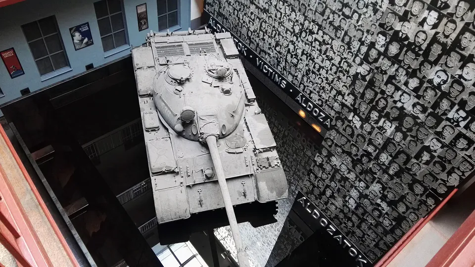 Soviet tank displayed in museum courtyard with wall of victim photographs in background
