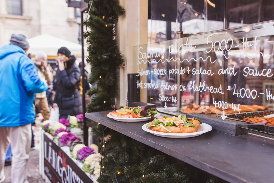 Traditional Hungarian lángos displayed at street food vendor with menu board and customers