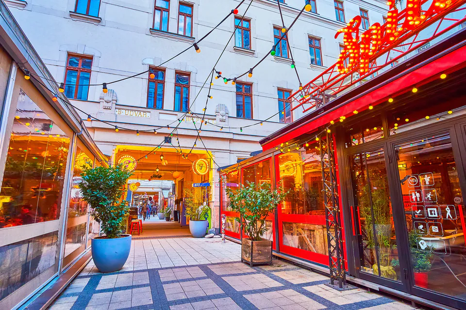 Illuminated courtyard passage with string lights, potted plants and colorful storefronts