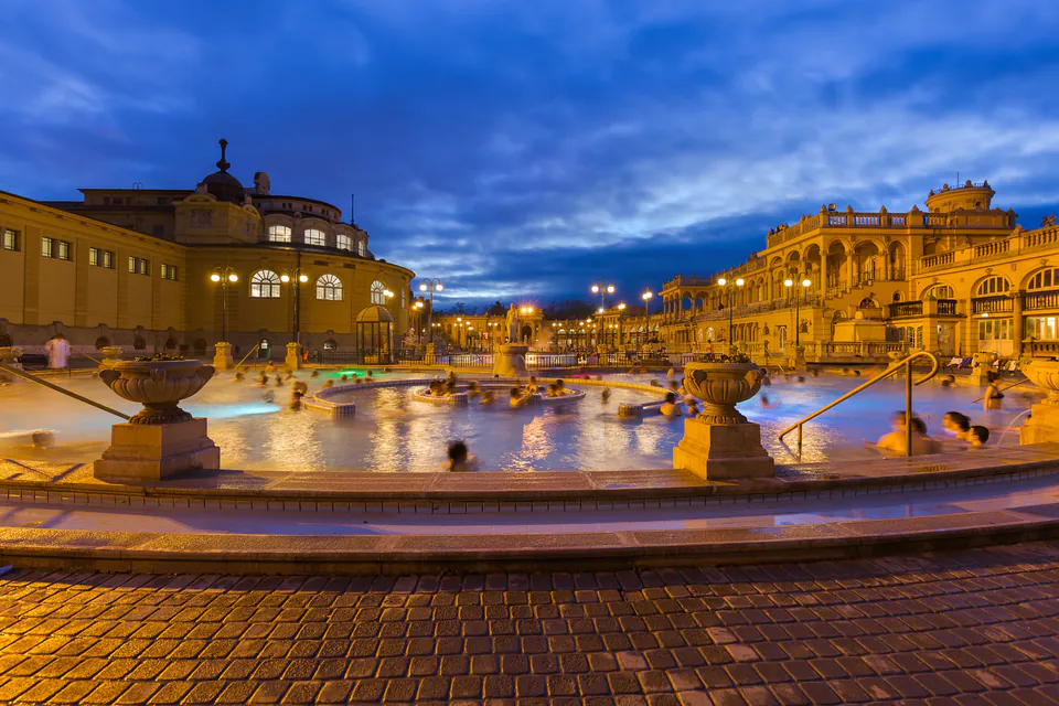 Széchenyi thermal baths illuminated at night with people relaxing in steaming pools