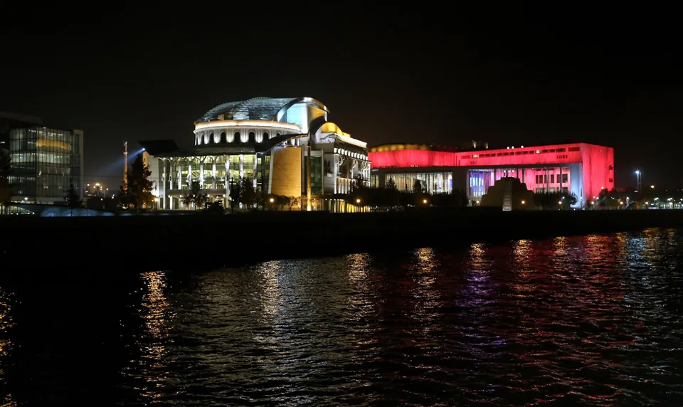 Illuminated Müpa cultural complex and National Theatre buildings reflecting colorfully in the Danube at night