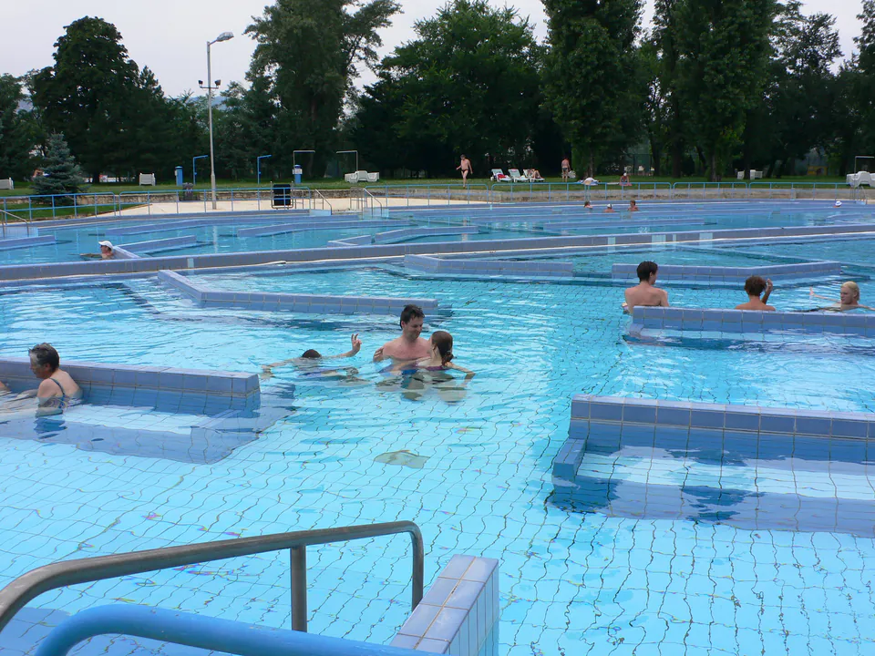 Multiple outdoor swimming pools with divided sections and people enjoying thermal waters