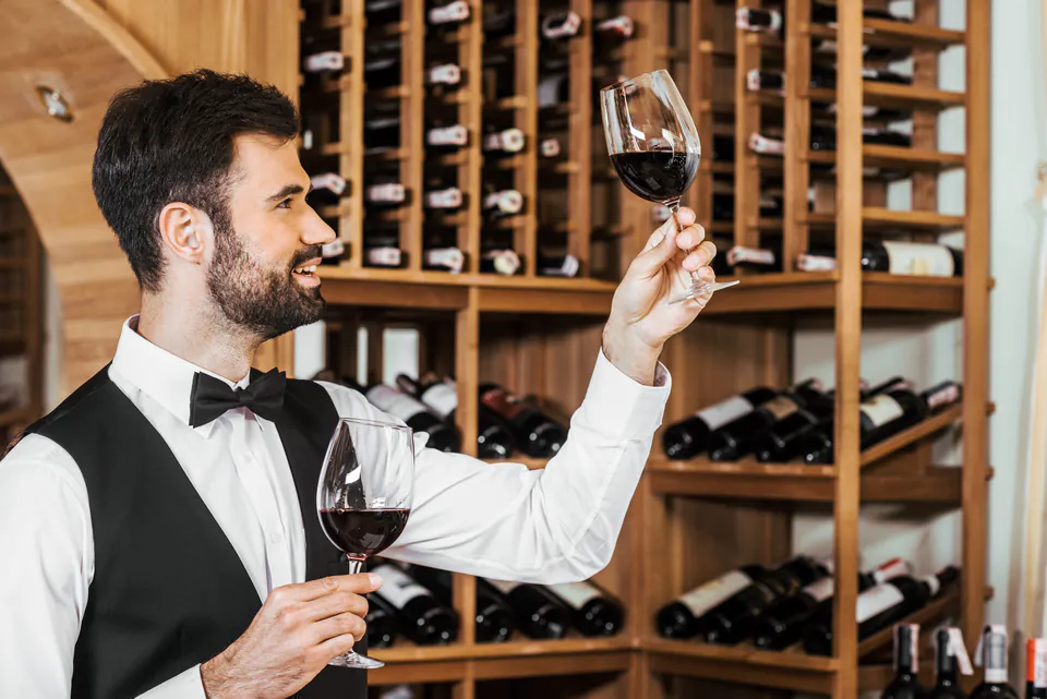 Wine expert examining glass in front of extensive wooden wine storage shelves