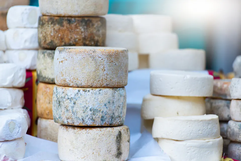 Stacked artisanal cheese wheels in various stages of aging displayed at market