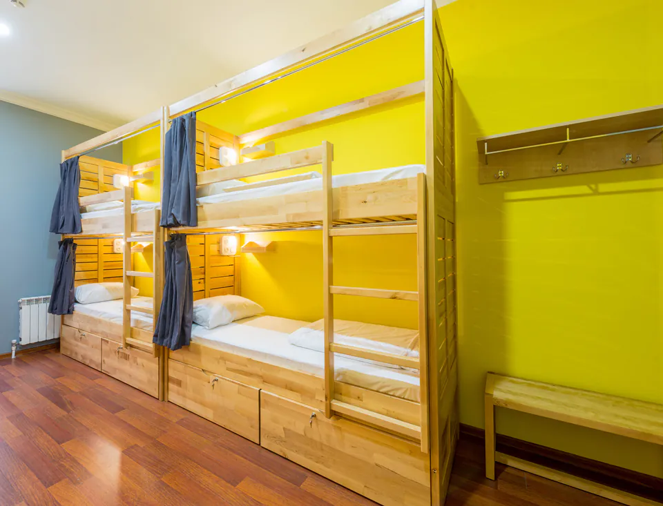 Modern hostel dorm room with wooden bunk beds, privacy curtains and storage against yellow walls