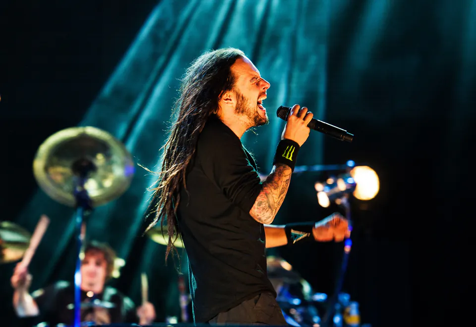 Performer singing passionately on stage with dramatic blue lighting and drummer in background