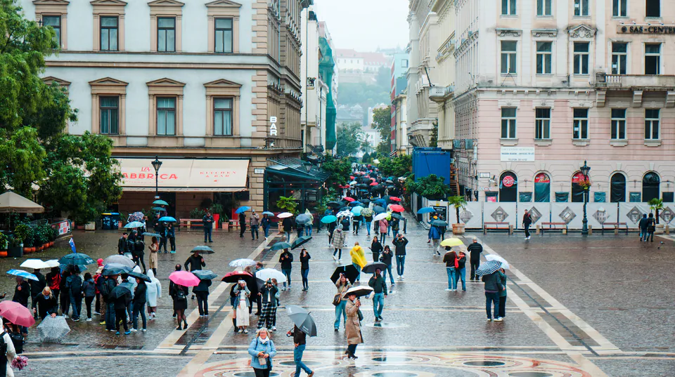 Pedestrians with umbrellas walking across Szent István Square in front of the basilica on a rainy day