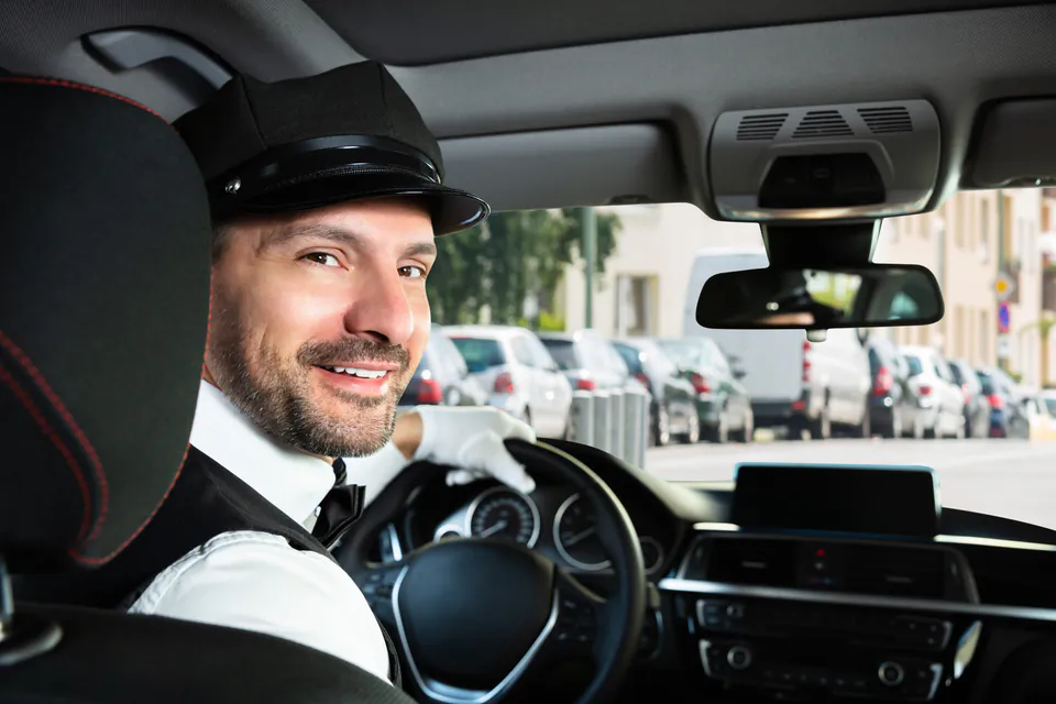 Professional chauffeur in uniform seated in luxury vehicle