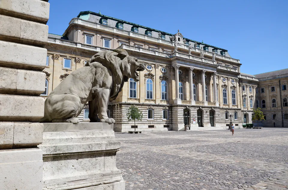 Stone lion statue guarding entrance to grand palace courtyard with ornate Baroque facade