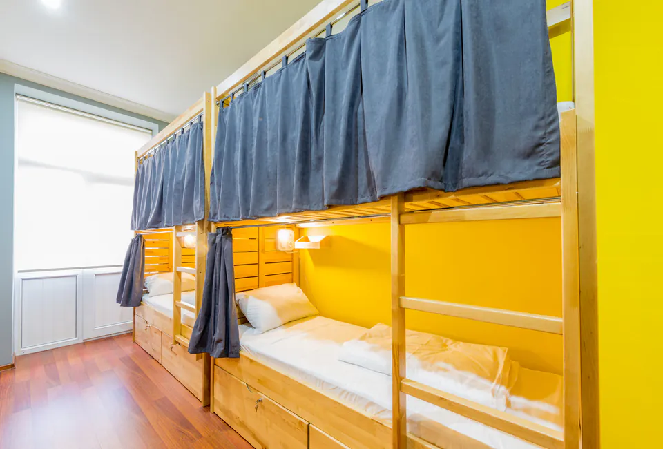 Modern dormitory room with wooden bunk beds, privacy curtains, and bright yellow walls