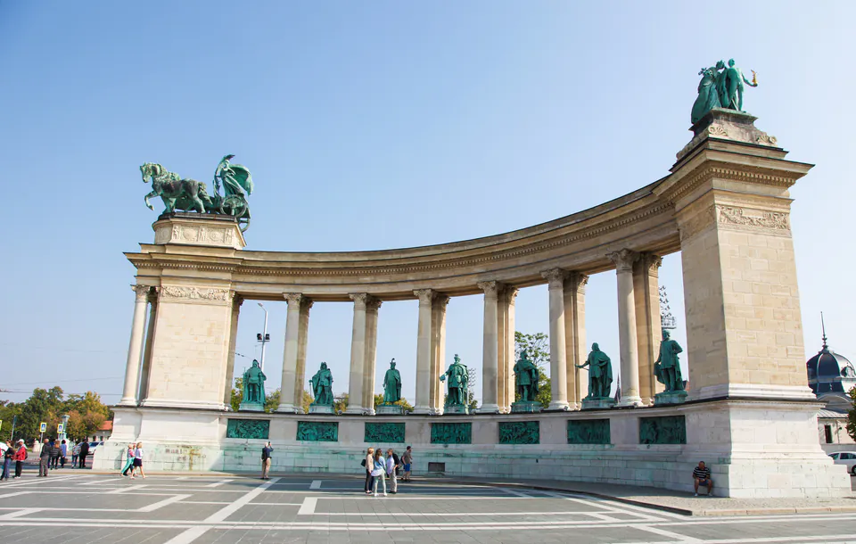 Semi-circular colonnade with bronze statues of Hungarian kings and historical figures set against blue sky
