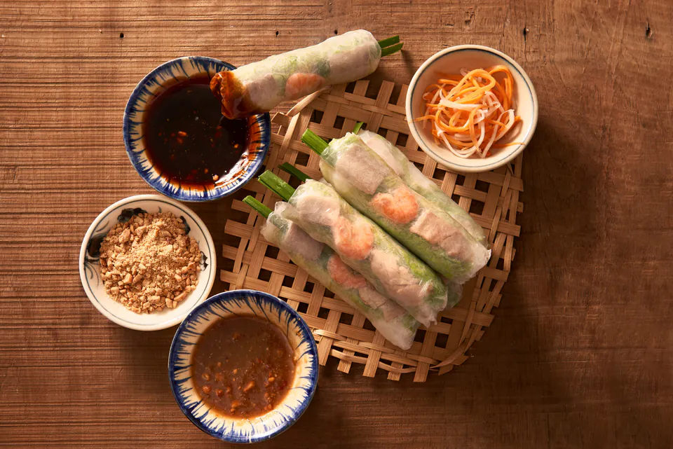 Vietnamese summer rolls served with dipping sauces and garnishes on bamboo mat
