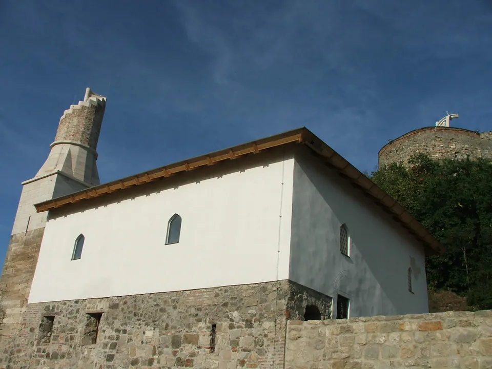 White two-story mosque with stone foundation and minaret against blue sky near Veprech Tower