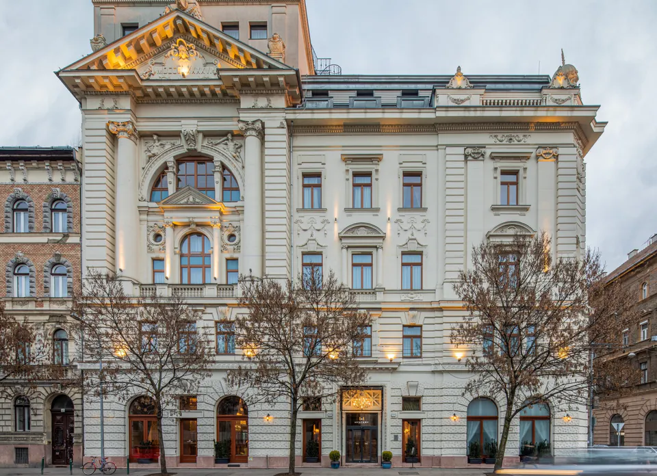 Ornate neoclassical building facade with illuminated arched windows and decorative stonework at dusk