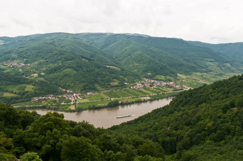 Scenic Danube River valley with lush green hills, riverside villages, and a boat