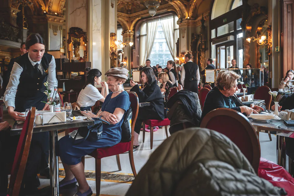 Historic café interior with ornate chandeliers, marble tables, and elegant décor
