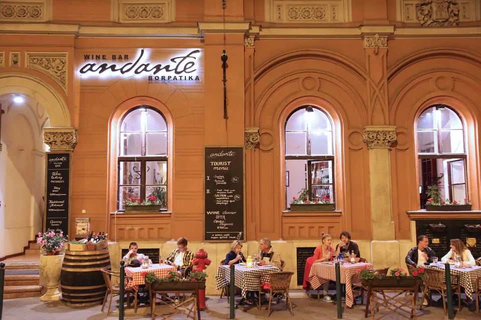 Evening diners seated at outdoor tables of Andante wine bar under arched building facade