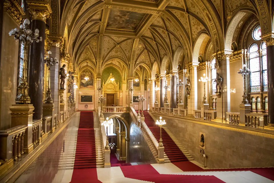 Grand marble staircase with red carpet, gilded arches, and ornate vaulted ceilings in Parliament building