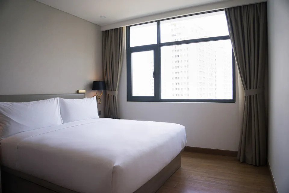 Modern hotel room with white bed linens, large window, and gray curtains
