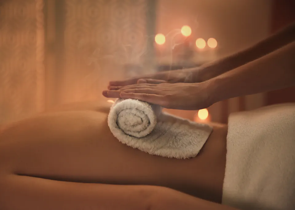 Massage therapy session showing hands working with warm towel in dimly lit spa room
