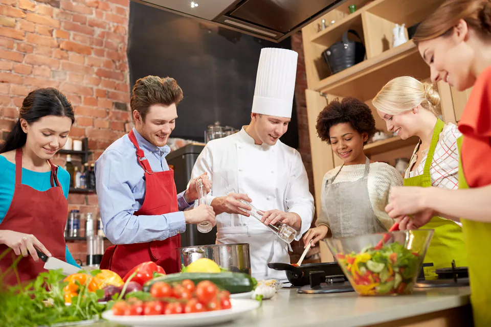 Small group of students learning cooking techniques from professional chef in kitchen setting