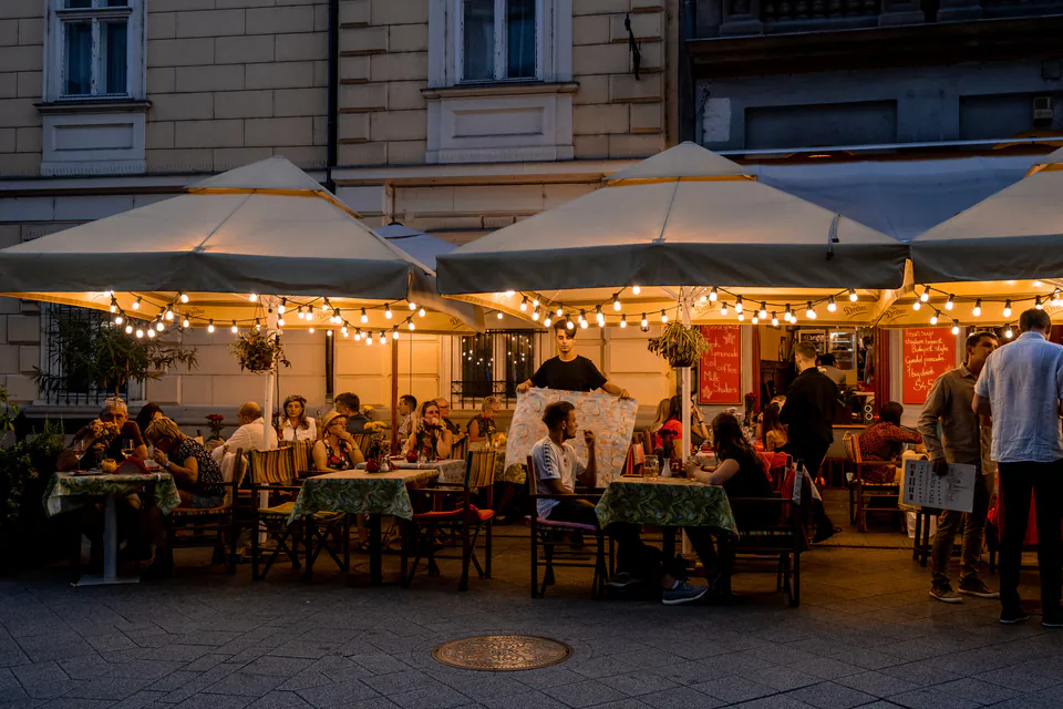 Evening outdoor dining scene with illuminated umbrellas and people enjoying dinner at restaurant tables